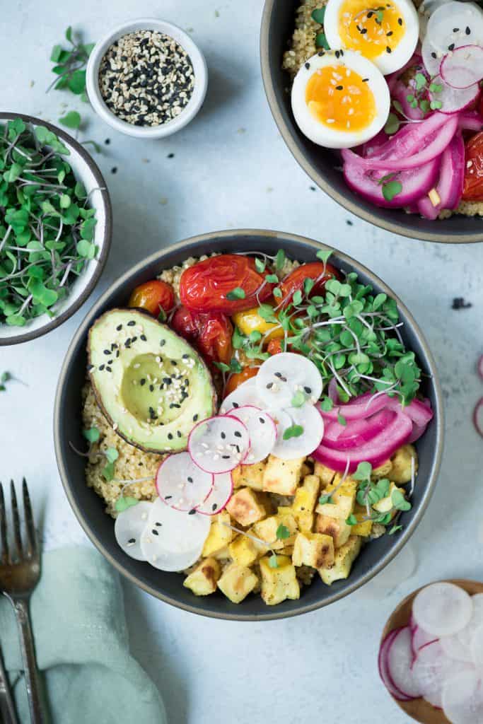 Close up Overhead of two bowls of breakfast quinoa with avocado, radishes, scrambled tofu, soft-boiled eggs and microgreens