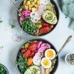 Overhead of two bowls of breakfast quinoa with avocado, radishes, scrambled tofu, soft-boiled eggs and microgreens
