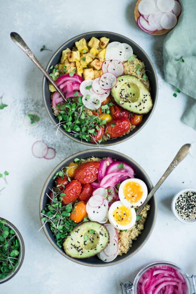 Overhead of two bowls of breakfast quinoa with avocado, radishes, scrambled tofu, soft-boiled eggs and microgreens