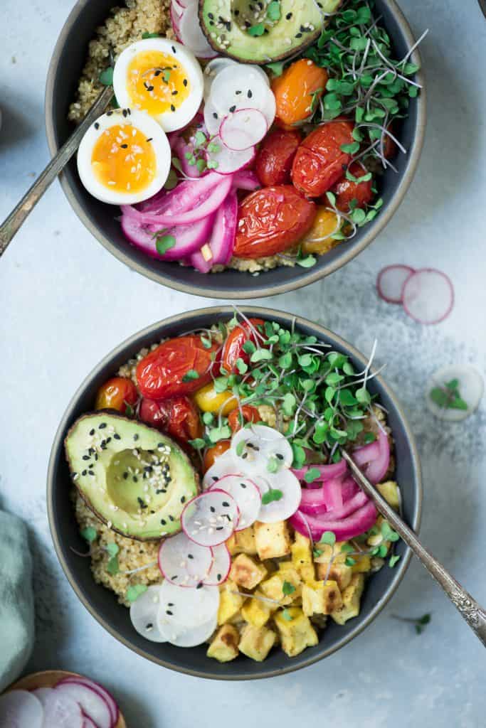 Close up Overhead of two bowls of breakfast quinoa with avocado, radishes, scrambled tofu, soft-boiled eggs and microgreens
