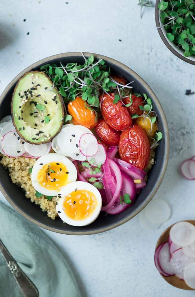 Close up Overhead of two bowls of breakfast quinoa with avocado, radishes, scrambled tofu, soft-boiled eggs and microgreens