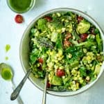 Overhead of corn, arugula and tomato summer salad in a white bowl with two large spoons