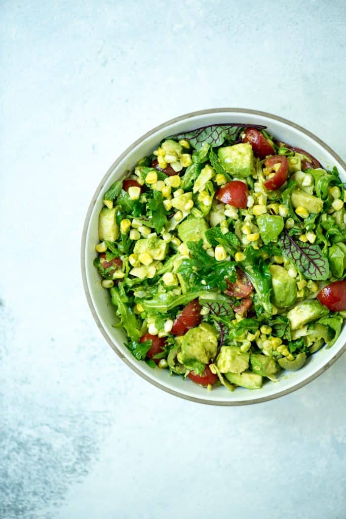 Overhead of corn, arugula and tomato summer salad in a white bowl on a white bowl