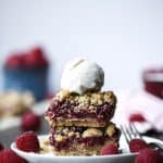 Stacked raspberry oatmeal crumble bars with a scoop of vanilla ice cream and fresh raspberries on a small white plate