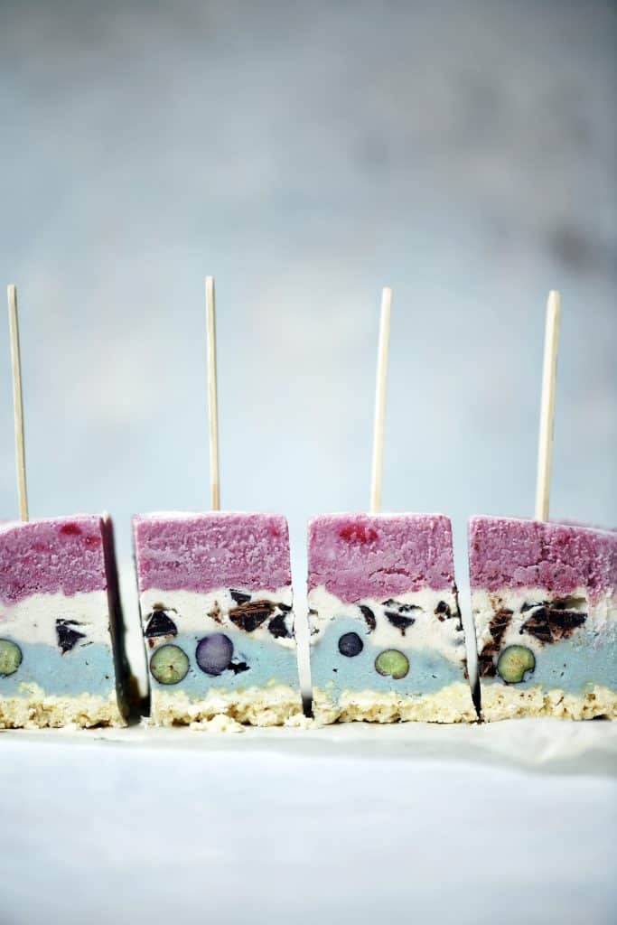 Side view of red white and blue layered ice cream pops standing up on a white surface