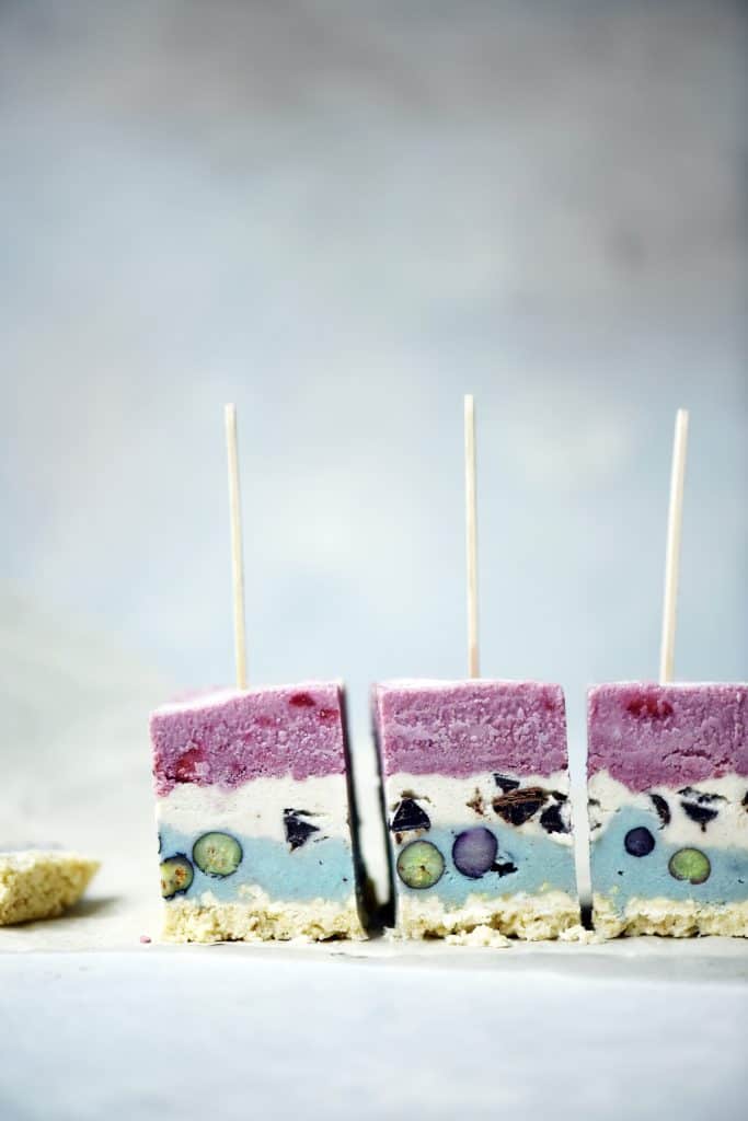 Side view of red white and blue layered ice cream pops standing up on a white surface
