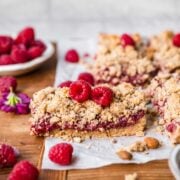 close up side view of raspberry crumble bar topped with fresh raspberries on parchment paper.