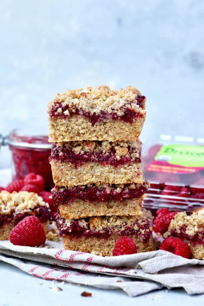 Stacked raspberry oatmeal crumble bars with fresh raspberries in background