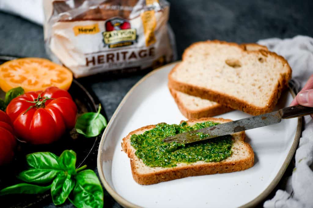 Spreading pesto onto gluten free bread on a white plate