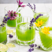 Green cocktail in cocktail glasses garnished with flowers.