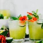 Side view of green cocktail with key limes and flowers