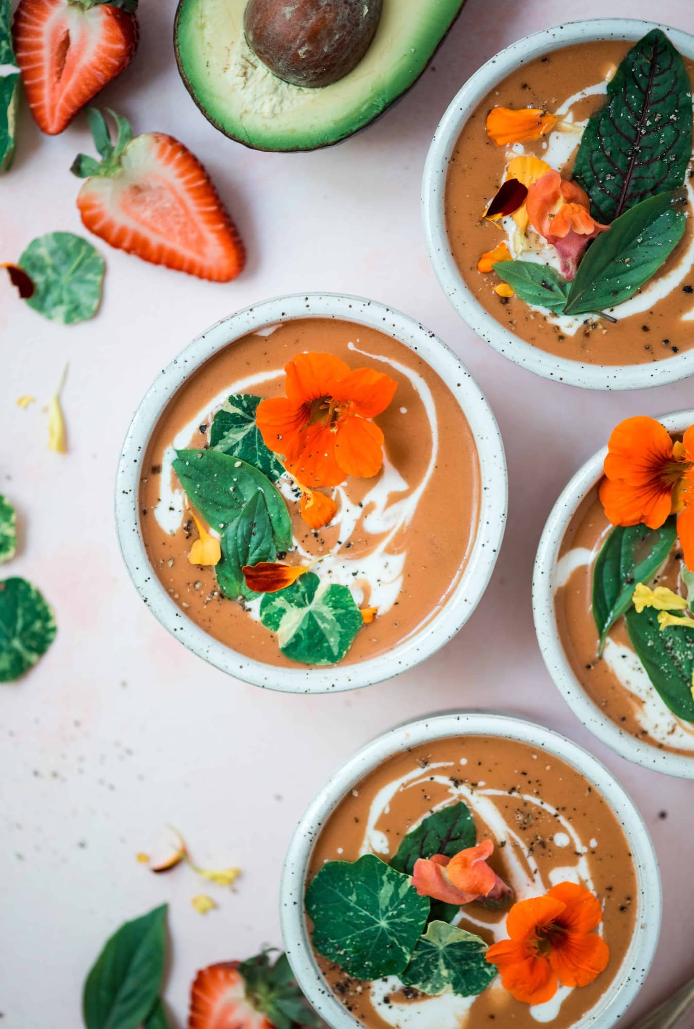 Overhead of 4 bowls of strawberry watermelon gazpacho on a pink background