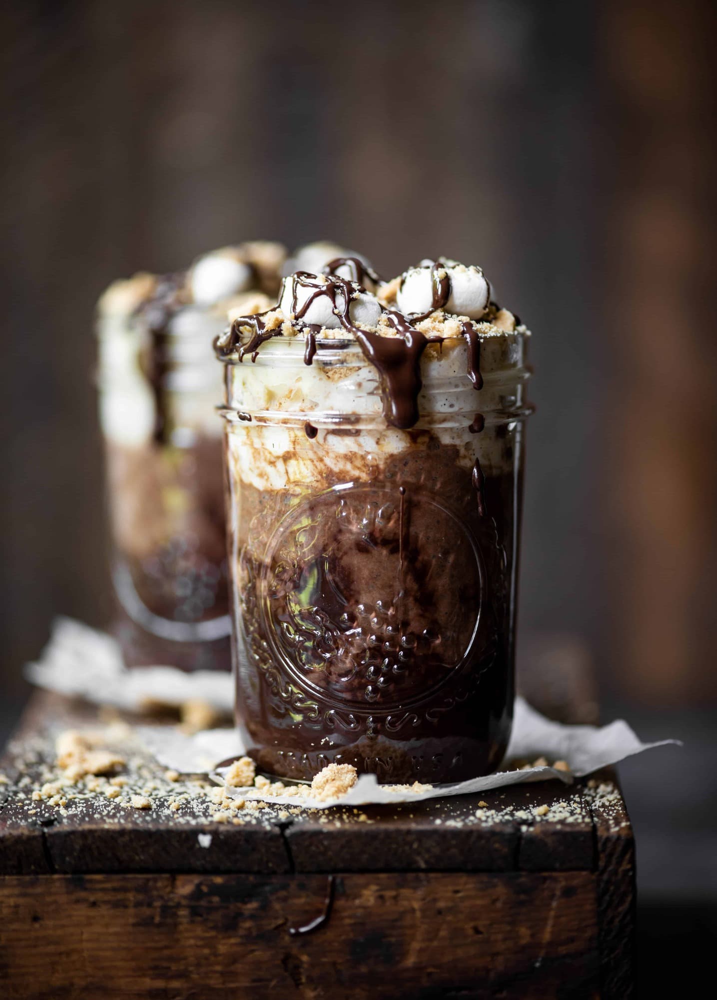 Side view of s'mores overnight oats drizzled with chocolate and marshmallows on a rustic wood board