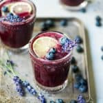 Side view of blueberry lavender margarita garnished with fresh blueberries and lavender on an antique serving tray