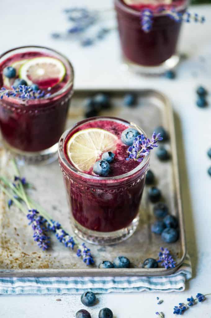 Side view of blueberry lavender margarita garnished with fresh blueberries and lavender on an antique serving tray