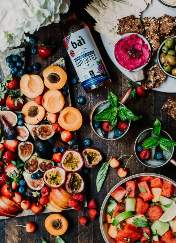 Overhead of fresh summer fruit board and berry moscow mules with fresh basil styled on a rustic wood background