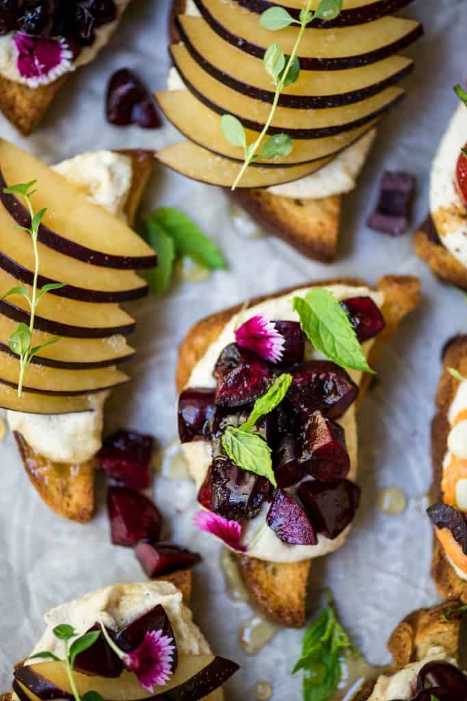 Close up of crostini topped with cherries, plum, ricotta and herbs