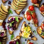 Overhead of crostini topped with ricotta, herbs, tomatoes, cherries and plums