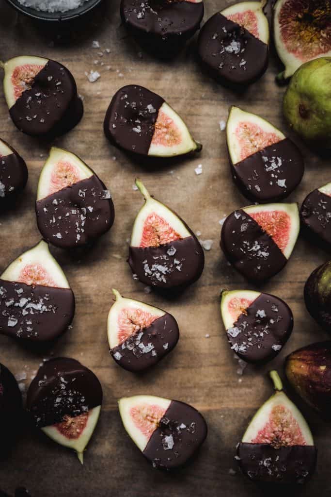 Overhead of dark chocolate dipped figs with sea salt on a white background