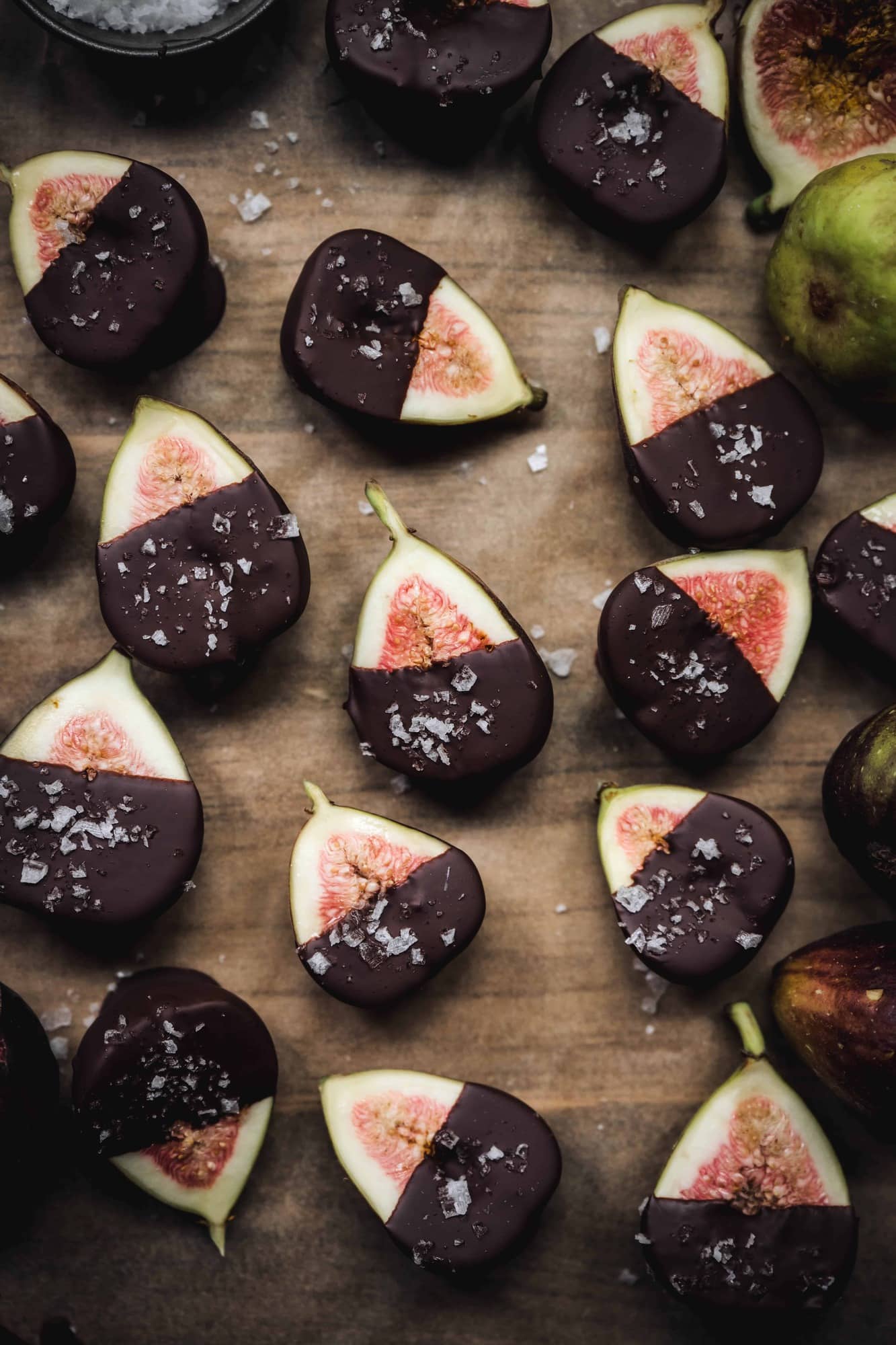 Overhead of dark chocolate dipped figs with sea salt on a white background