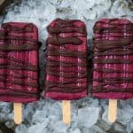 Overhead of three red popsicles drizzled with chocolate over crushed ice on a tray