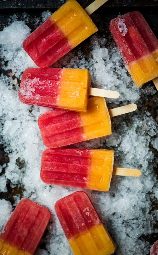 Watermelon Peach Prosecco Popsicles on a sheet pan filled with crushed ice