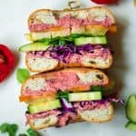 Overhead of rainbow veggie bagel sandwich with beet hummus sliced in half on a white tray