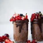 Side view of chocolate mocha overnight oats in a glass jar with dark chocolate drizzle and fresh summer berries. Styled on a white background