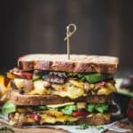 Side view of two stacked fajita paninis with veggies and vegan cheese on a rustic wood cutting board