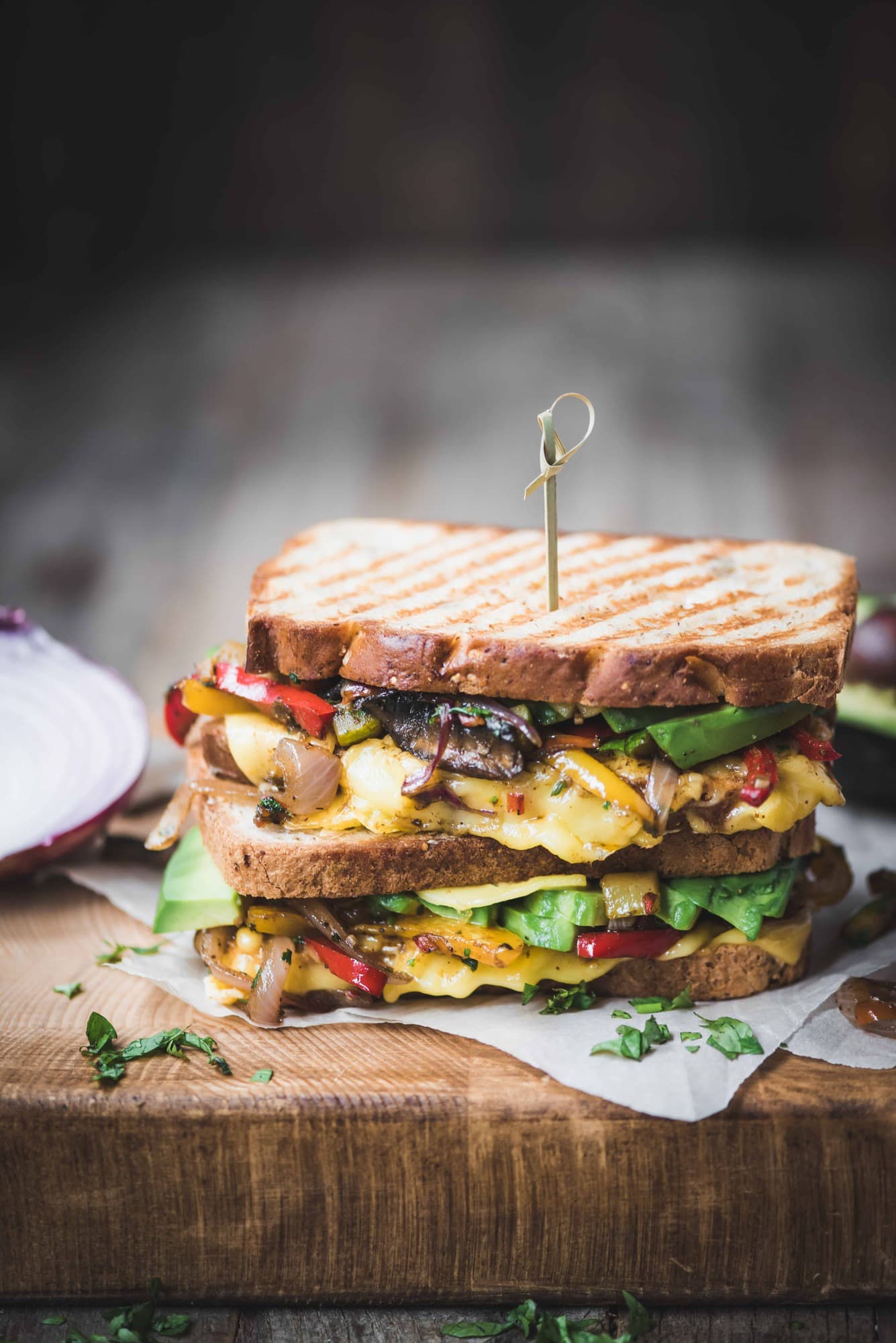 Side view of two stacked fajita paninis with veggies and vegan cheese on a rustic wood cutting board