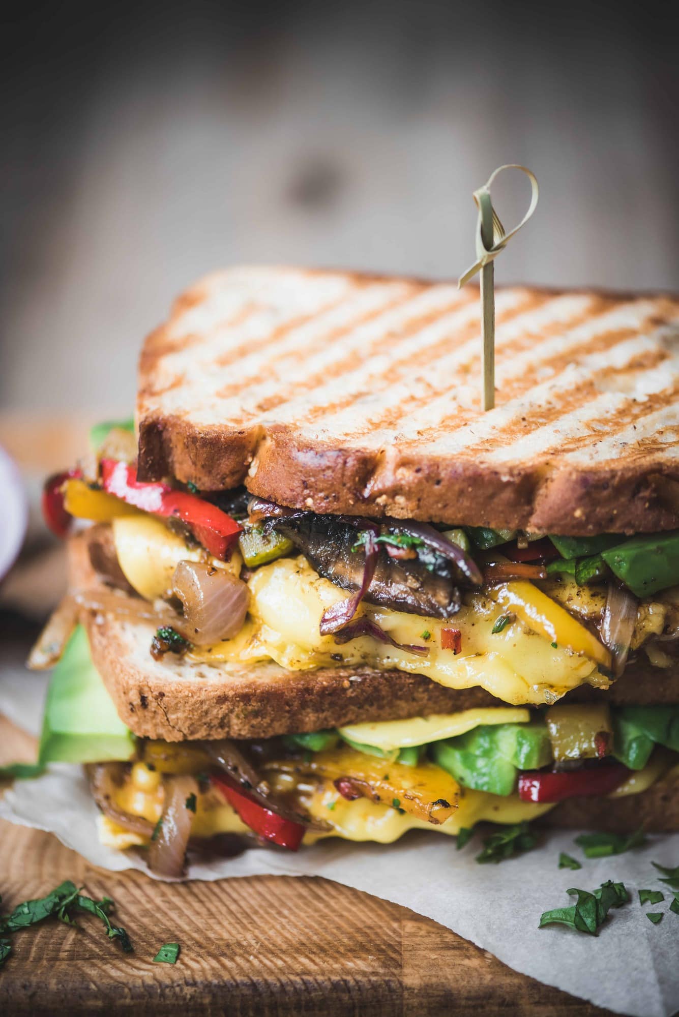 Close up Side view of two stacked fajita paninis with veggies and vegan cheese on a rustic wood cutting board