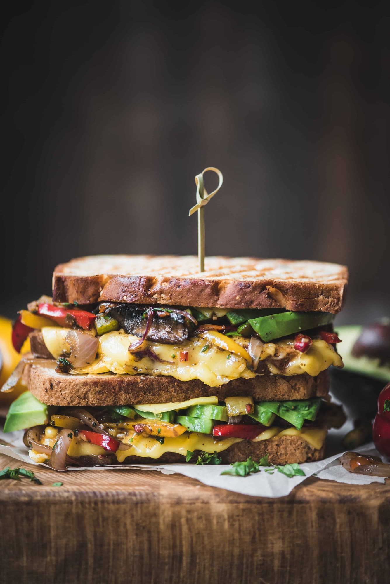 Side view of two stacked fajita paninis with veggies and vegan cheese on a rustic wood cutting board