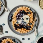 Overhead of lemon blueberry poppyseed waffles topped with whipped cream and blueberries on a white background