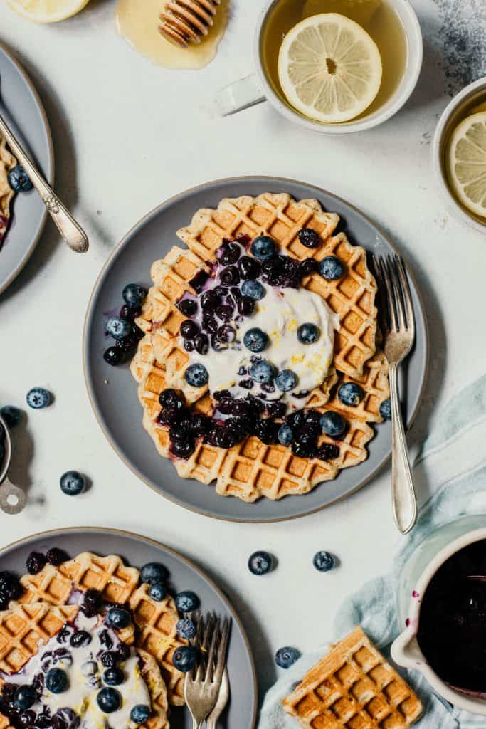 Overhead of lemon blueberry poppyseed waffles topped with whipped cream and blueberries on a white background
