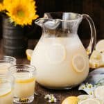 Side view of homemade lemonade in a large vintage pitcher on a wood surface with sunflowers in the background