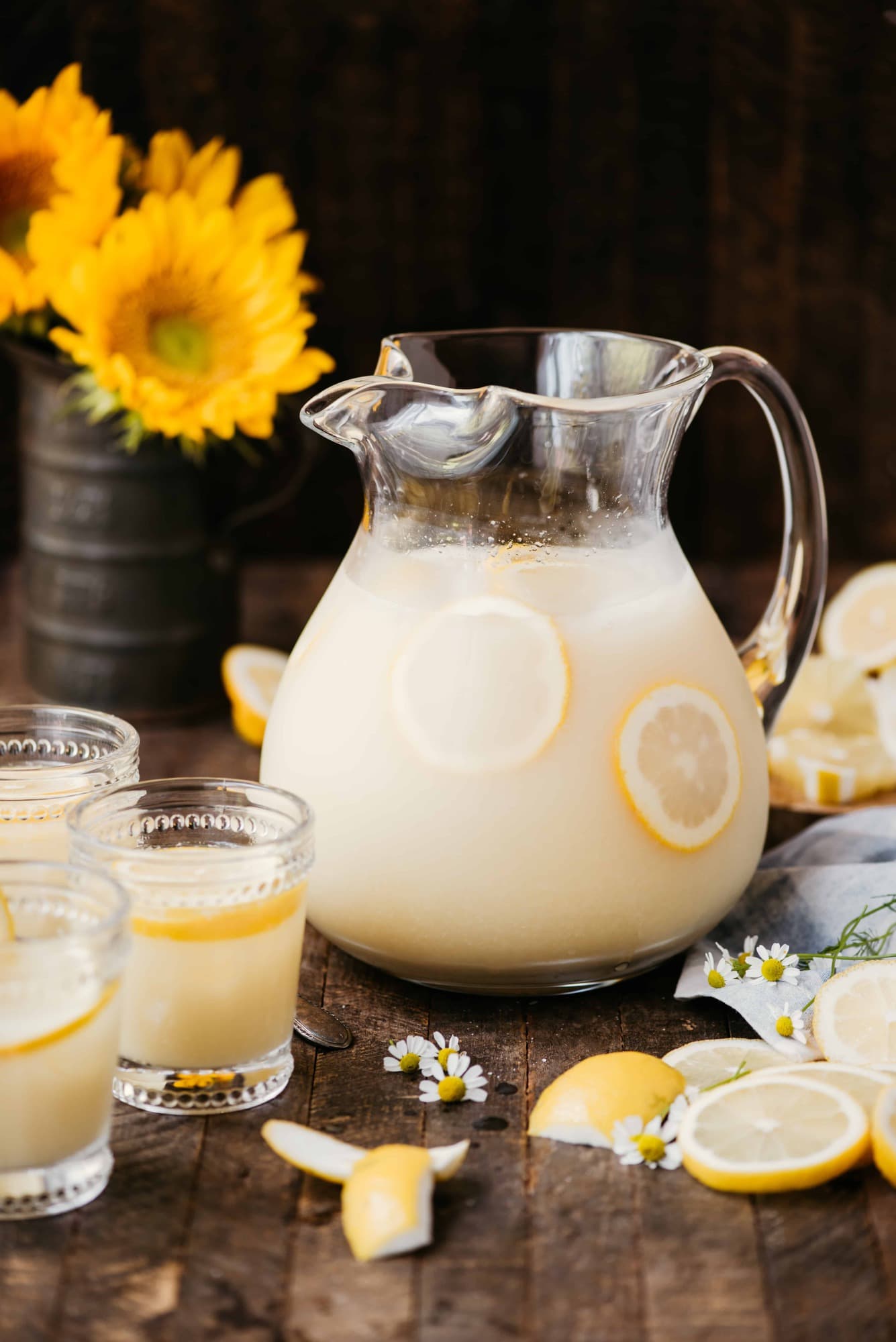 Side view of homemade lemonade in a large vintage pitcher on a wood surface with sunflowers in the background