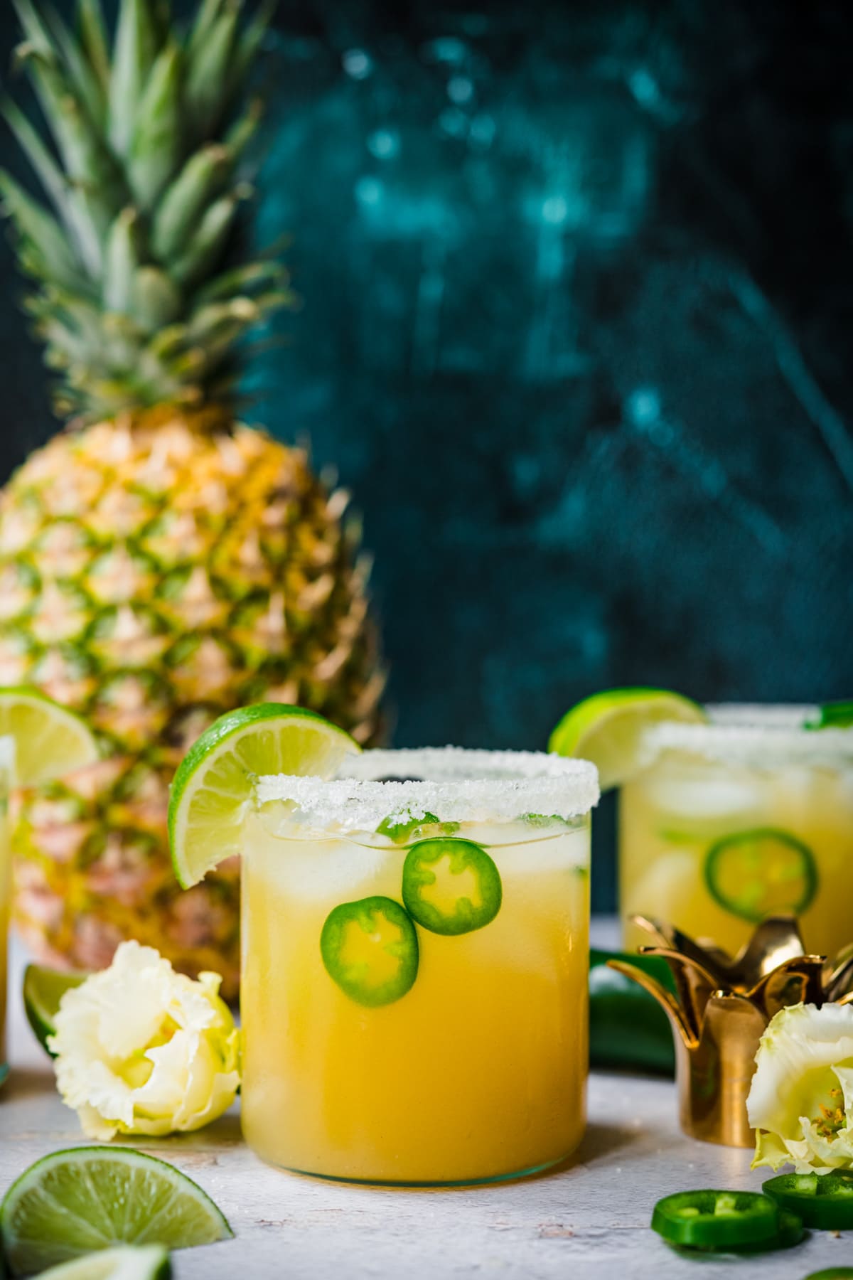 side view of pineapple jalapeño margarita in glass rimmed with salt with a fresh pineapple in background. 