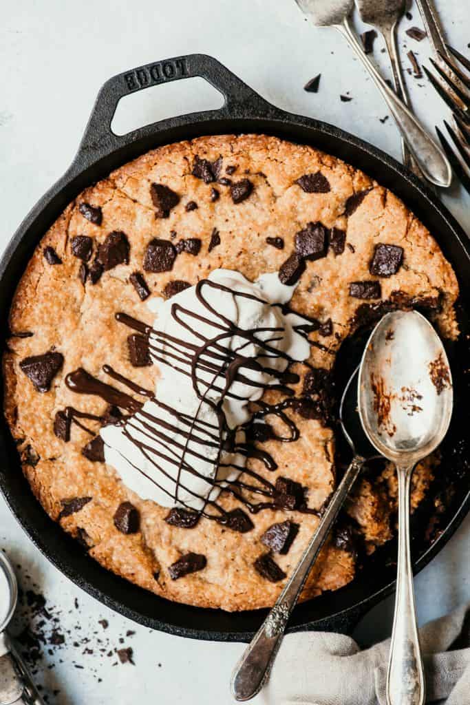 Close up overhead of a giant chocolate chunk skillet cookie topped with vanilla ice cream and chocolate sauce