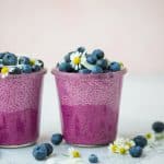 Side view of ombré pink pitaya chia pudding topped with fresh blueberries, coconut and white and yellow flowers