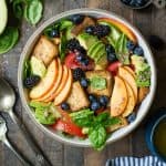 Overhead of Peach Blueberry Panzanella in a white bowl with avocado and fresh basil