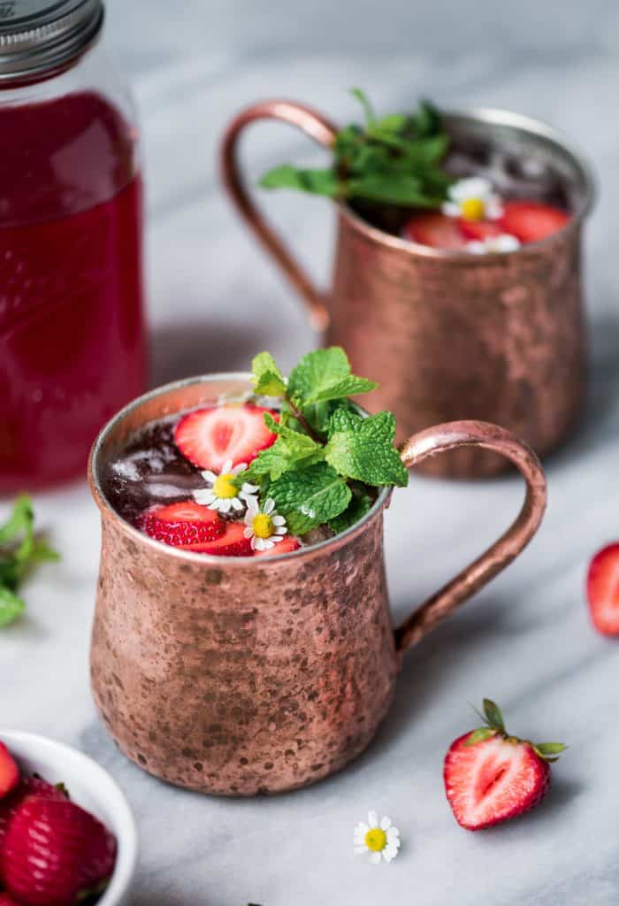 Close up of strawberry moscow mules in copper mugs on marble background