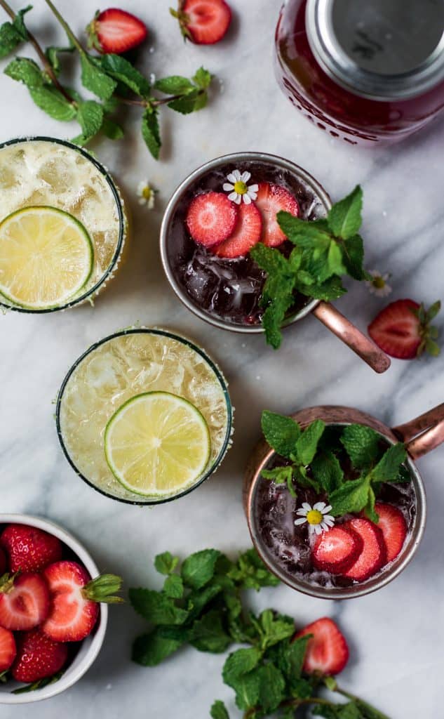 Overhead of pineapple jalapeño margaritas and strawberry moscow mules on a marble background