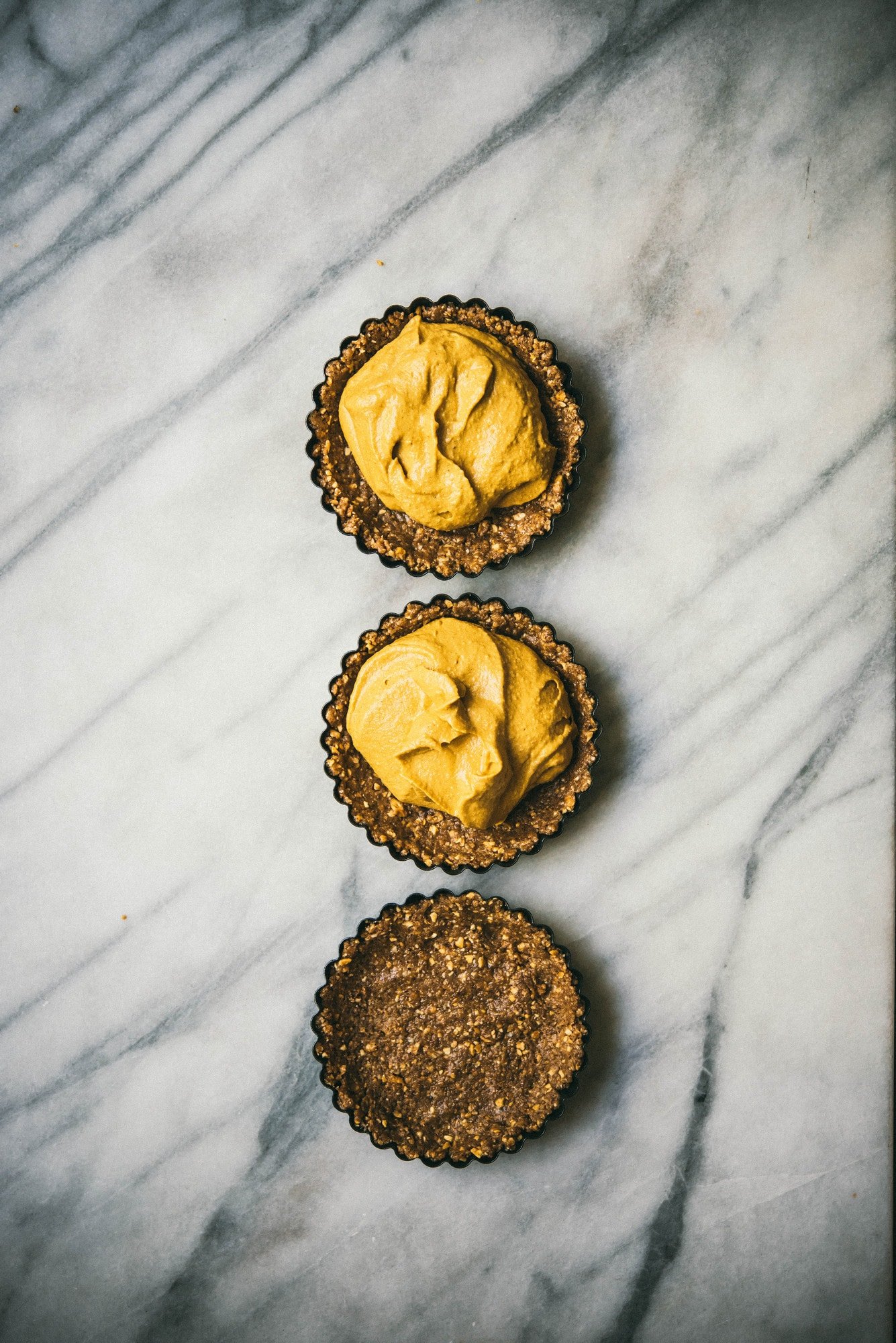 3 mini pumpkin cheesecake tarts on marble surface