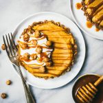 Overhead of mini pumpkin cheesecake topped with caramel and whipped cream on a white plate on a white marble surface