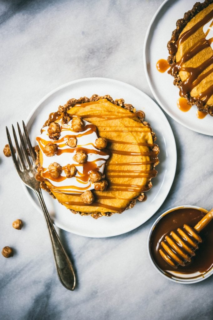 Overhead of mini pumpkin cheesecake topped with caramel and whipped cream on a white plate on a white marble surface