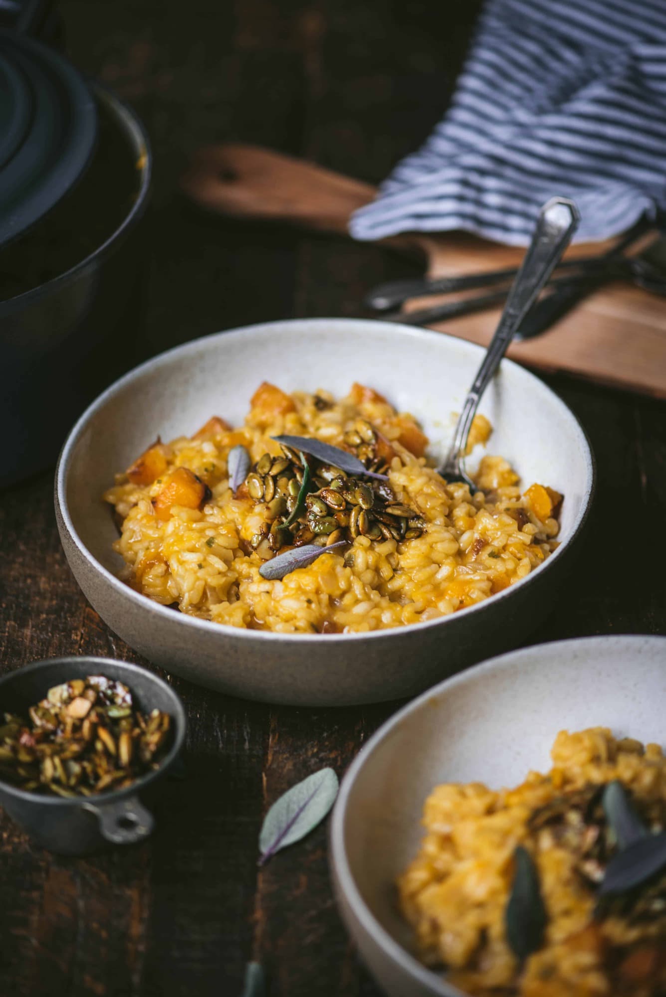 Side view of two bowls of butternut squash risotto with fresh sage. On a rustic wood background