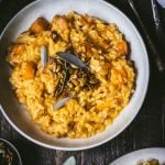 Overhead of white bowl of butternut squash risotto topped with fresh sage and candied pepitas