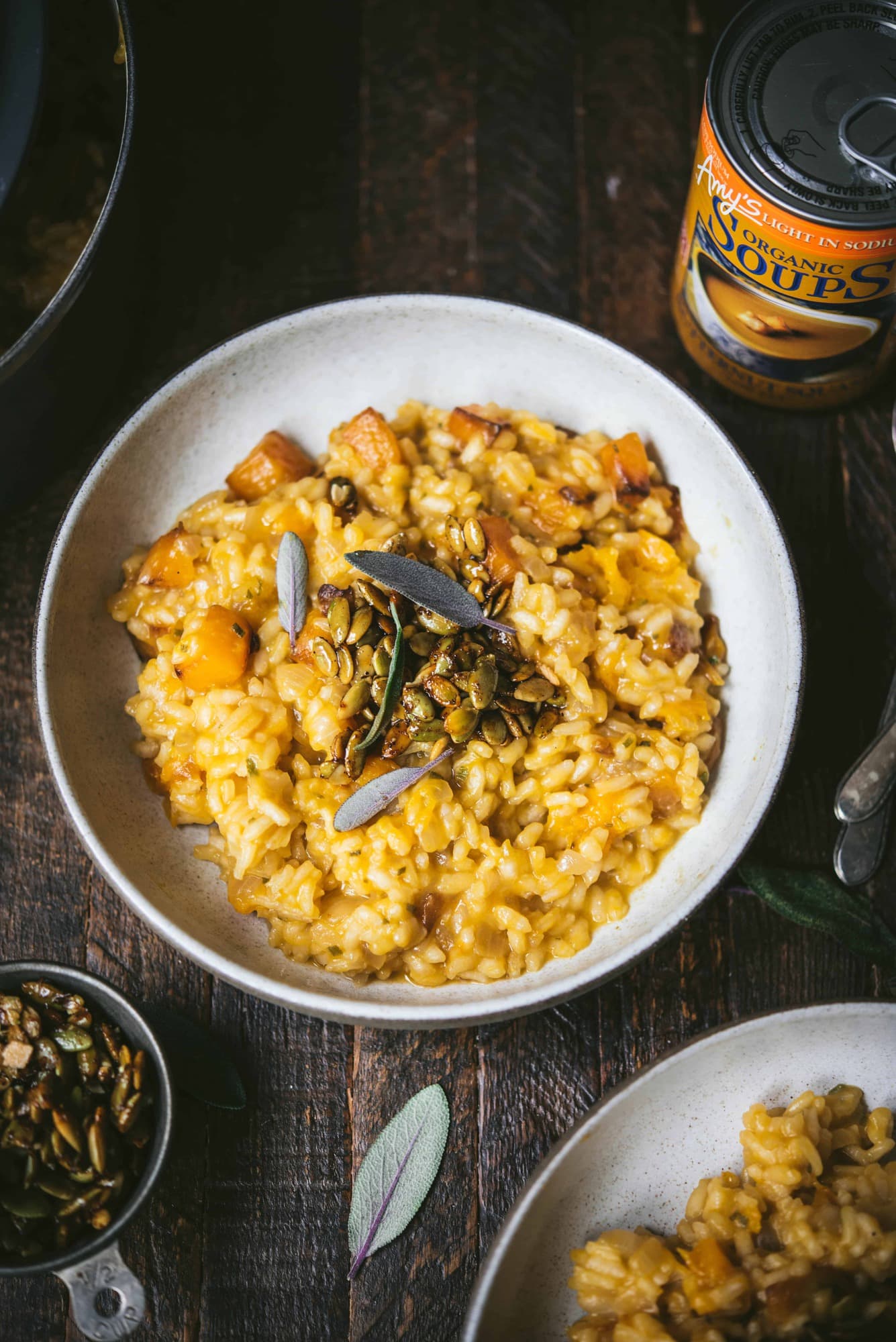 Overhead of white bowl of butternut squash risotto topped with fresh sage and candied pepitas