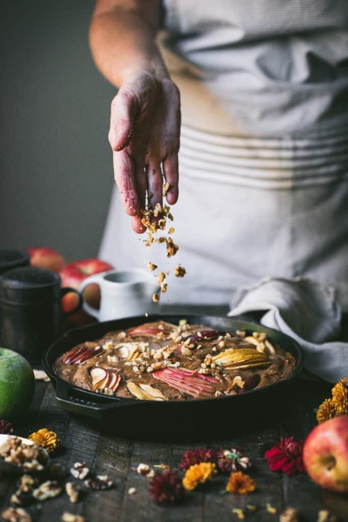 Pouring chopped nuts over an apple cake in a cast iron skillet