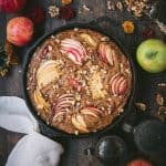 Overhead of an apple walnut cake in a cast iron skillet surrounded by fall flowers and apples